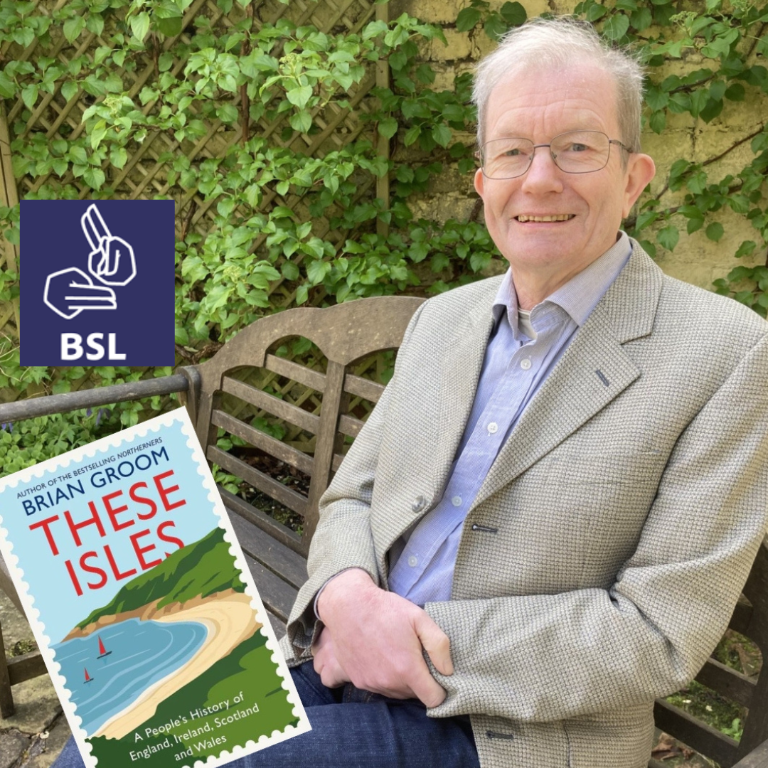 A man wearing glasses and a light brown tweed jacket sits on a wooden bench in front of a trellis covered in ivy, holding a book titled "These Isles" by Brian Groom. A dark blue square with a white British Sign Language (BSL) logo and the letters "BSL" is in the upper left corner.